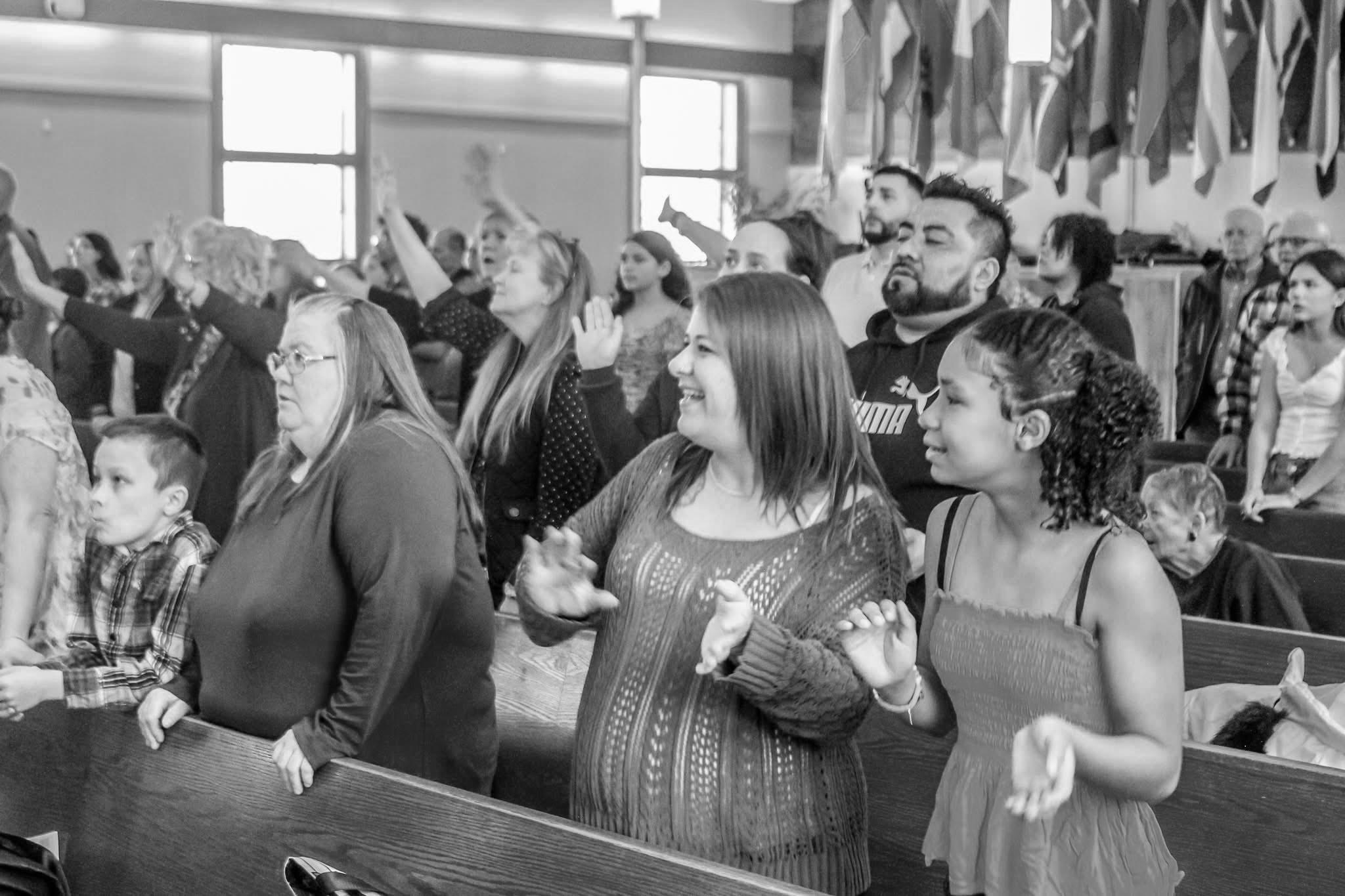 Congregation worshipping together, hands raised, with flags of the nations represented in the church displayed above